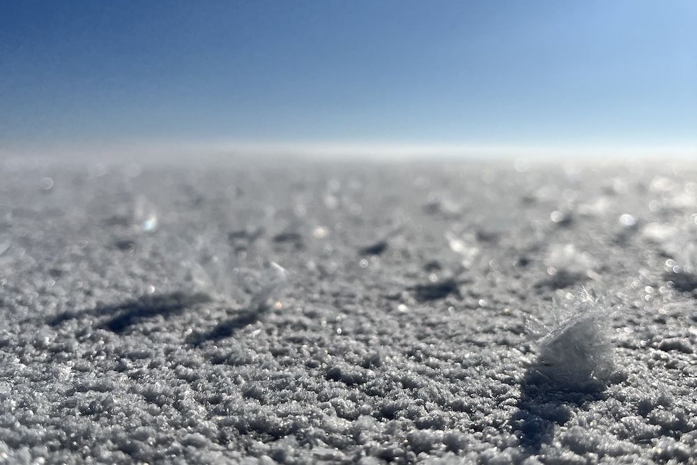Close up of snow and snow flakes in front of a brig blue sky.